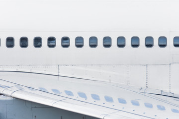 View of the fuselage of the aircraft and many windows, with reflection on the wing.