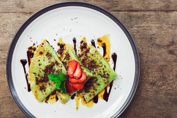 Traditional indonesian green pancakes topping with chocolate and strawberries slices. Breakfast...