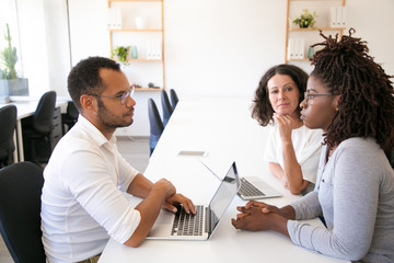 Diverse workgroup discussing and sharing ideas for project. Man and women in casual sitting at table with laptops and talking. Brainstorming concept