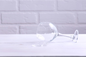 Broken wine glass on a white wooden table against the background of a loft. Broken, old dishes.