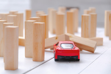 The red toy car overcomes all obstacles in the way and barriers reaching the goal and knocking down obstacles in its path. A red car rides and knocks down wooden poles in its path.