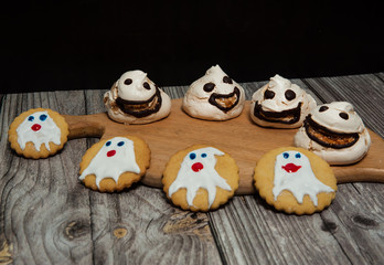 Homemade cakes for Halloween. Scary and horrible ghosts meringue and cookies with ghosts on wooden background.
