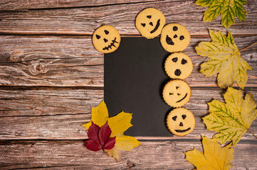 Composition for Halloween. Black paper blank, tasty homemade cookies, autumn leaves on a wooden background.