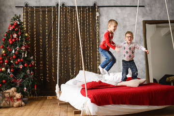 Obraz na płótnie Canvas boys, brothers, have fun. jumping on hanging bed, in room with Christmas tree cluttered with red balls