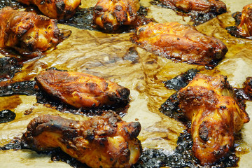 Close up of roasted spicy chicken wings on baking tray and cooking paper.
