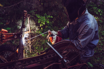 Man using welding machine stick to cut melt iron metal construction outdoors, wearing protective...