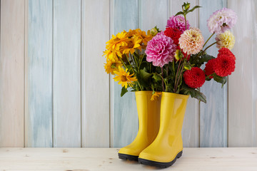 Yellow rubber boots standing on a wooden background of dirt and a flower inside