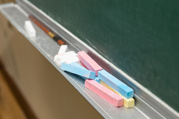 Closeup of blank green blackboard with pieces of coloured chalks