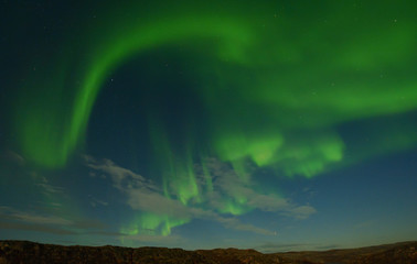 Northern lights, aurora in the sky above the hills and rocks at night.