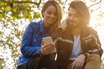 Young couple using cellphone in autumn colored park.