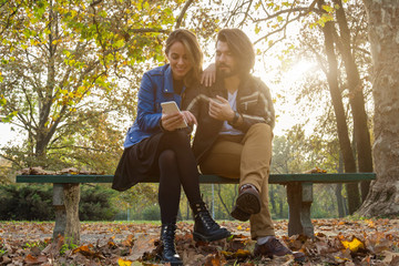 Young couple using cellphone in autumn colored park.