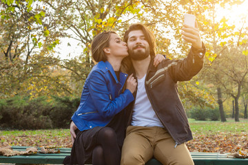Young couple using cellphone in autumn colored park.