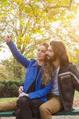 Young couple using cellphone in autumn colored park.