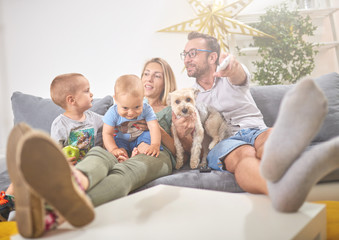 Young parents watching TV with baby boy and a dog.