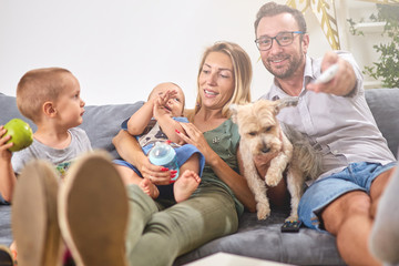Young parents watching TV with baby boy and a dog.