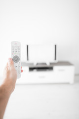 Hand holding TV remote controller with a modern television set.