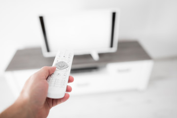 Hand holding TV remote controller with a modern television set.