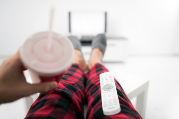 Man drinking soda juice and looking at TV with legs on the table in living room.