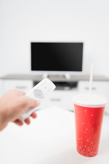Hand holding TV remote controller with a soda juice and TV.