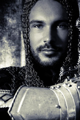 Portrait of handsome medieval knight in suit of armour with beard and blue eyes looking at camera