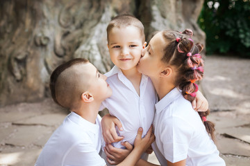 three happy joyful cute children wearing white shirts. lovely girl is kissing her small brother in the park. concept of love and family