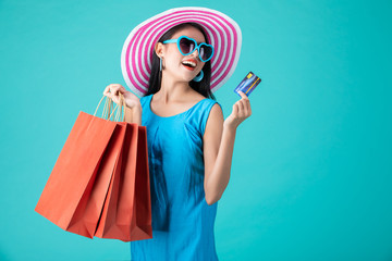 Portrait of a happy Asian pretty girl holding shopping bags while Hold Credit Cards looking away isolated over blue background,colorful shopping concept. 