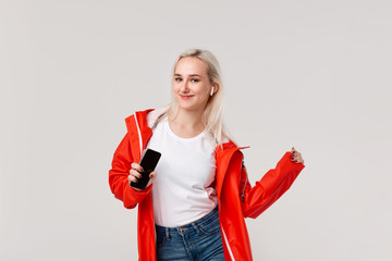 Pretty blond girl wearing red raincoat and white t-shirt dancing  listening to music with wireless earbuds. Concept of enjoying life.