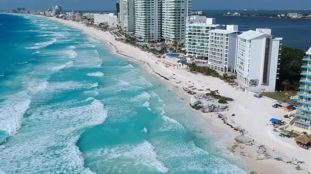 Aerial shot of the hotel zone in canc&uacute;n, in a sunny day hitting the blue waters of the caribbean. Pan from the waves to the hotels.