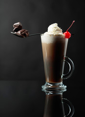 Layered coffee cocktail with whipped cream, cherry and pieces of chocolate.
