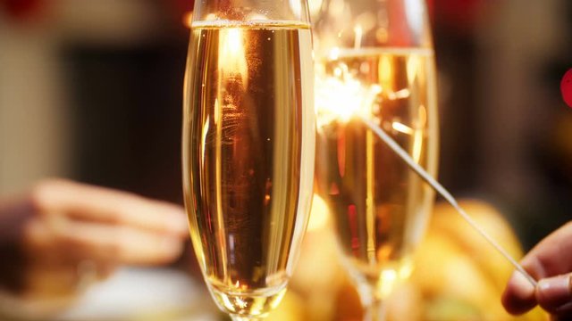 Closeup 4k footage of romantic couple holding sparkler next to glasses of fizzy champagne. Family celebrating Christmas and New Year holidays