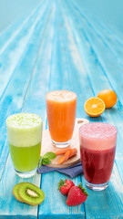 Different Juices in One Group Picture Includes Kiwi Juice, Strawberry Juice, Orange Juice with Carrots Juice. On Blue Wood Background Giving Tropical Refreshing Feel. Three Fruit Juices in Glasses