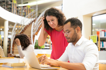 Serious colleagues working with laptop at library. Two students working with laptops together. Education concept