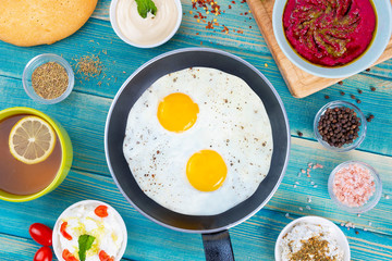 Eggs in Pan with Bread and Hummus and Labneh with Cup of Tea with Limon. On Blue Wood Surface, Perfect Breakfast Meal, Fried eggs in a frying pan