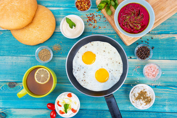 Eggs in Pan with Bread and Hummus and Labneh with Cup of Tea with Limon. On Blue Wood Surface, Perfect Breakfast Meal, Fried eggs in a frying pan