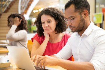 Concentrated people reading information from laptop. Cheerful students working with laptop at library. Education concept