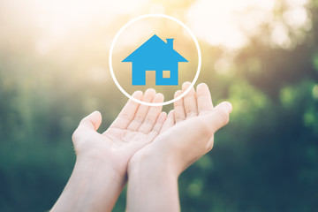 Woman open hand up to sunset sky and green blur leaf bokeh sun light with home icon abstract background. Business finance and family life concept.