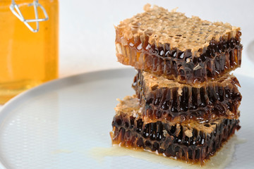 honeycomb with honey lie on a gray plate next to a jar of honey and a honey spoon, selective focus