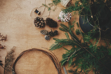 Details for workshop of making christmas wreath. Fir branches, pine cones, thread, scissors, wooden circle, berries and herbs for rustic wreath on wooden table. Making christmas wreath