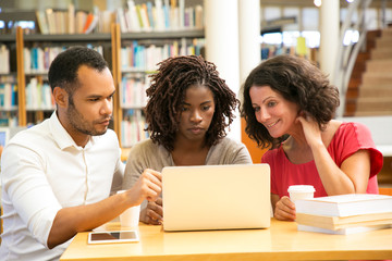 Front view of tired mature students looking at laptop. Thoughtful man and women sitting at table...