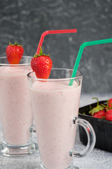 Two glasses with strawberry milkshake with pieces of berries on the edge of the glass on gray background.