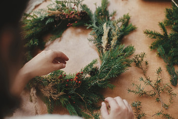 Making rustic Christmas wreath. Hands holding fir branches, and pine cones, thread, berries on wooden table. Christmas wreath workshop. Authentic stylish still life © sonyachny