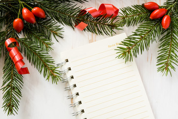 Background for Christmas and new year cards with a branch of spruce, red berries, and a note book on white background. Copy space.