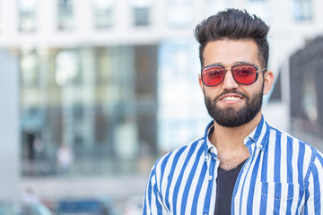 Portrait of cheerful positive stylish student guy in glasses with a mustache and beard outdoors. The concept of successful cheerful people.