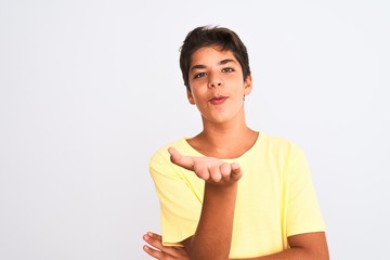 Handsome teenager boy standing over white isolated background looking at the camera blowing a kiss with hand on air being lovely and sexy. Love expression.