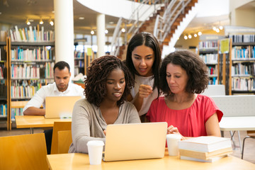 Smiling women working with laptop at public library. Cheerful students working over new project at library. Education concept