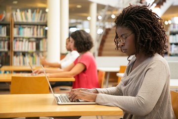 Focused female customer using public wi-fi hotspot in library. Young African American woman sitting...