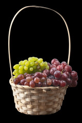 fresh juicy brushes of grapes of different varieties in a wicker basket isolated on a black background