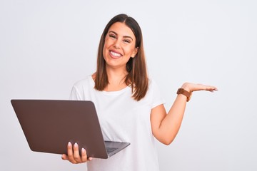 Beautiful young woman working using computer laptop over white background smiling cheerful presenting and pointing with palm of hand looking at the camera.