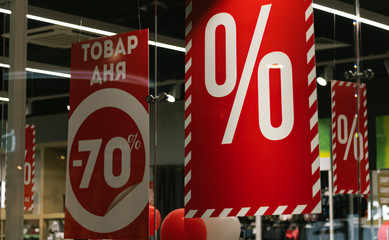 Product of the day -70%. Sale red signs in a clothing supermarket. More percent discounts price in a boutique window glass.