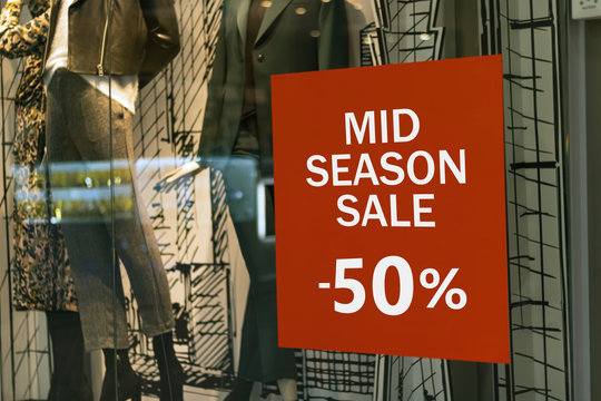 Mid season sale -50% red sign in a clothing supermarket. More percent discounts price in a boutique window glass.